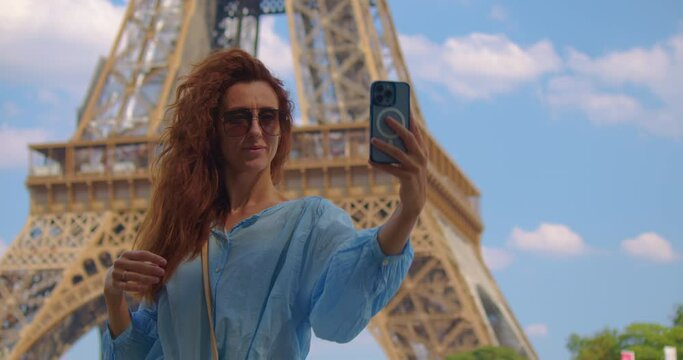 Parisian woman taking a photo on a smartphone. Cinematic footage of a young woman wearing fashionable clothes having fun in Paris at the eiffel tower park and streets. Concept about european tourism