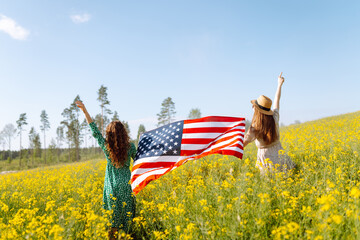 Two Young woman with american flag on blooming meadow. 4th of July. Independence Day. Patriotic...