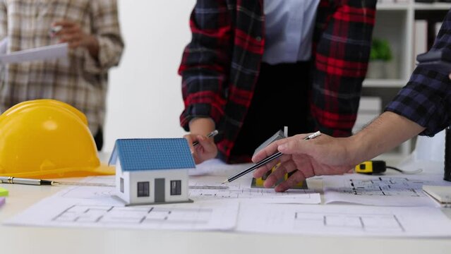 Group of professional architects brainstorm together to work on the design of a house construction project on blueprints in the office.