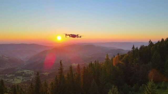 Aerial view of drone flying over pine forest taking footage of colorful sunset in wild mountains. Beautiful nature landscape illuminated with bright setting sun