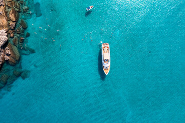 Aerial top down view of a swimming tourists and yacht anchored in the turquoise sea