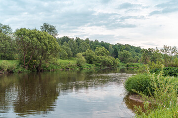 Beautiful green summer landscape of a meadow near a river and a forest. a small river running through the field.