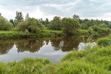 Beautiful green summer landscape of a meadow near a river and a forest. a small river running through the field.
