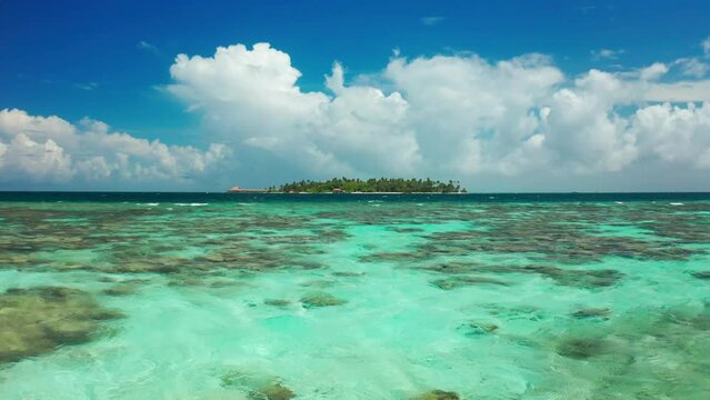 Above fly view on water and tropical island with the turquoise sea, coconut palm trees and deep blue sky in the Maldives islands.