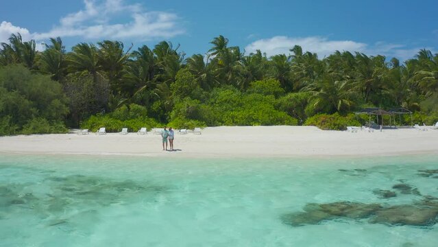 Romantic couple taking a stay on the white sand beach with turquoise water sea in Thinadhoo island, Maldives.