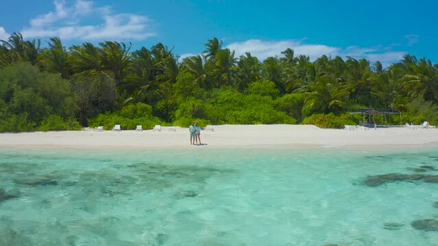 Romantic couple taking a stay on the white sand beach with turquoise water sea in Thinadhoo island, Maldives.