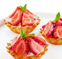 Tartlets with custard, strawberries and mint served on white plate