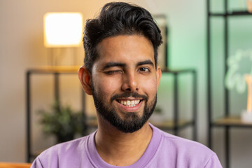 Smiling playful happy young indian man blinking eye, looking at camera with smile, winking and...