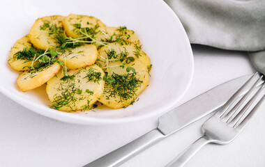Fried potato slices with dill on a white plate