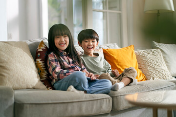 portrait of two cute asian children brother and sister sitting on family couch looking at camera...