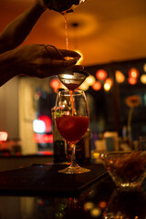 Barman gently pours the finished cocktail from glass shaker into glass at night club.