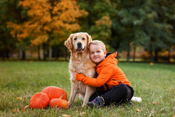 Happy joyful little boy walking with his dog golden retriever in a beautiful autumn forest with...