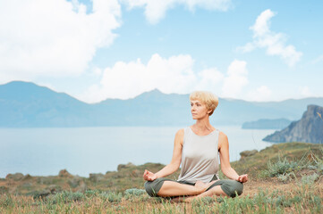 Fototapeta na wymiar Senior woman doing yoga exercises with mountain and sky on the background