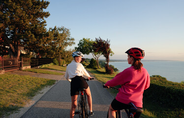 Two women riding on bicycle on the sea promenade. Back view.