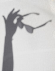 Shadow of a person holding a pair of sunglasses with his arm on a white background. Copy space. Summer vacations concept.