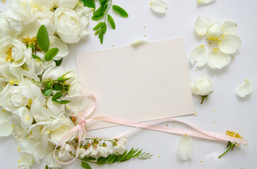 Obraz na płótnie Canvas Delicate composition of blank card with white roses and petals with acacia flowers and pink ribbon on white background. Wedding concept. Invitation card template