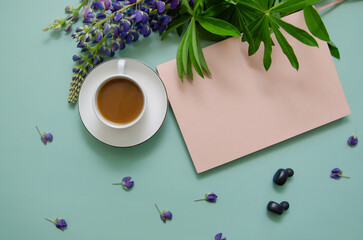 White cup of tea with lupine flowers and petals with rose paper notebook for text and earphones on blue background. Space for text or design.