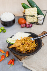 Indomie goreng sambal gami or spicy fried indomie is Traditional food from Indonesia. served on plate with a bowl of rice and vegetables. Isolated gray background