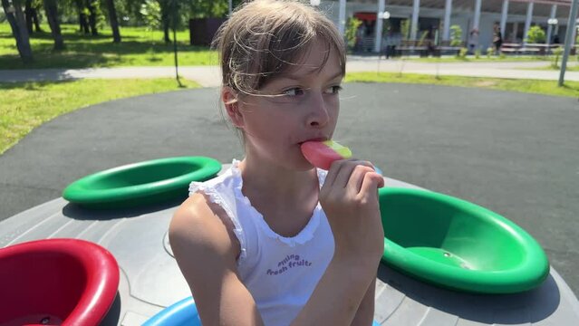 a happy child eats ice cream while relaxing in the park on a summer day, a brunette girl eats colorful ice cream, swings on a swing, has fun in an amusement park