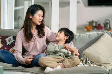 happy asian mother and son sitting chatting on family couch at home