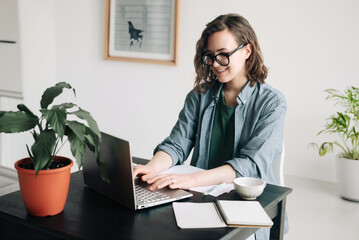 Young woman working on laptop in professional office setting. Student girl multitasking at home...