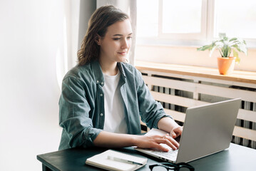 Young woman multitasking with a laptop in a modern office environment and student girl focused on work from home. Online work, study, freelance, business, and office lifestyle concept.