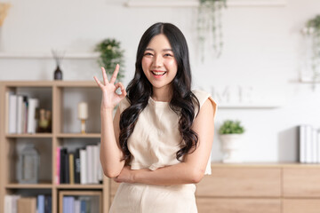 Beautiful young Asian woman showing thumbs up OK gesture smile with positive emotional at home....