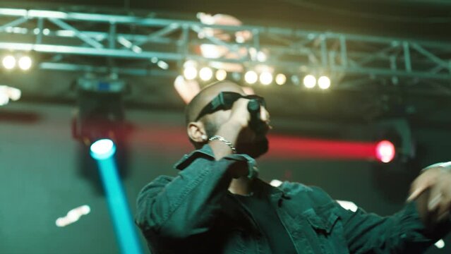 African-American Black rap artist performing his gig on a stage of a large venue, surrounded by bright flashig lights