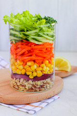 Healthy vegan salad with bulgur and vegetables in mason jar on wooden board with. White background. Side view