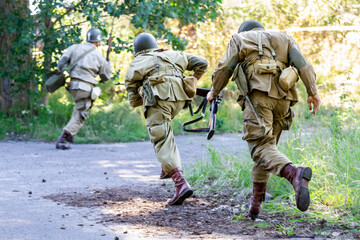 Historical reconstruction. An American paratrooper soldiers from the World War II  fighting in the forest. View from the back.