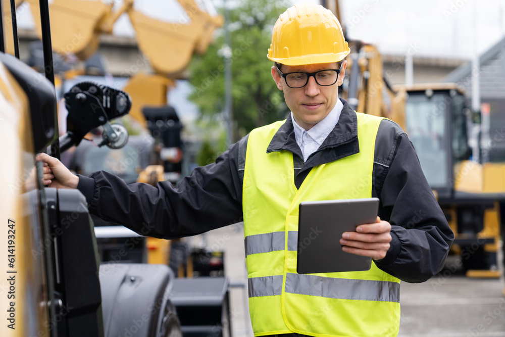 Poster Worker in a helmet with a digital tablet on the background of construction machine.