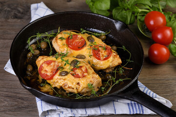Tender chicken breast baked with tomatoes, capers, herbs under cheese crust in a frying pan