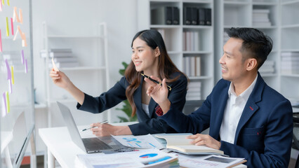 Two Young Asian business people discuss with new startup project Idea presentation, analyze planning and financial statistics and investment market at office.