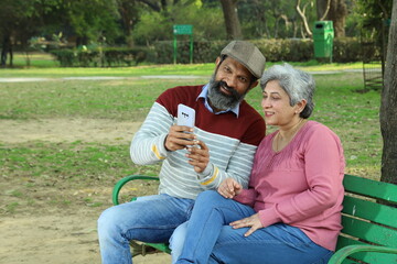 Young Indian Happy couple sitting on a park bench in a serene atmosphere taking a selfie