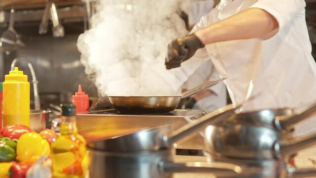Professional master chef frying pieces of meat in pan. Cook using special kitchen tools and preparing delicious dishes by prescription in restaurant commertial kitchen. Concept of culinary.