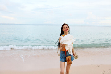 A young woman after swimming in the ocean with a backpack in wet clothes walks along the beach, summer vacation on an island by the ocean in Bali sunset