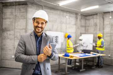 Portrait of structural engineer in business suit and hardhat holding tablet computer at...