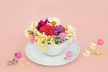 Surreal summer flower and wildflower teacup composition on pink background with scattered flowers....