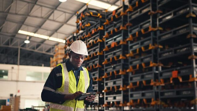African American man worker checks products stock inventory with digital tablet in the retail warehouse full of shelves Male employee wearing hard hat doing work in storehouse.