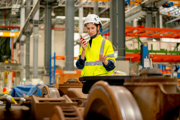 Fototapeta premium Profession engineer or technician worker use walkie talkie to contact with co-worker or team staff and look to wheel and stand behind part of electric train in maintenance center.