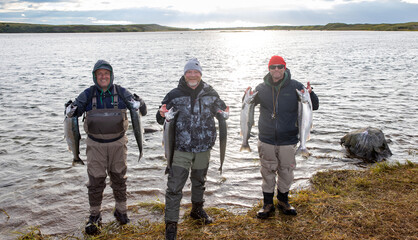 Three brothers holding their fresh catch of coho salmon on the shore of the Egegik river in Alaska