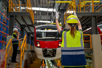 Obraz na płótnie Canvas Technician or factory worker woman stand and show action to the driver in electric train in factory workplace and co-worker also stay near the train.