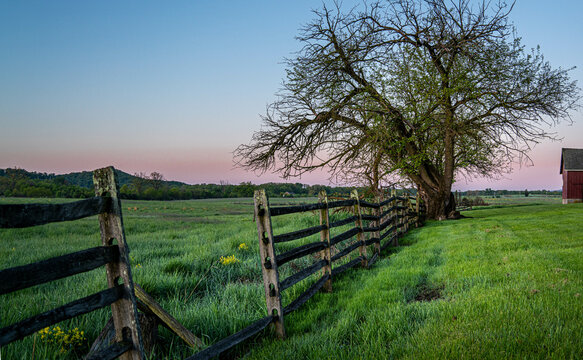 A morning sunrise lights a field in Gettysburg with green grass and an old fence in the countryside.