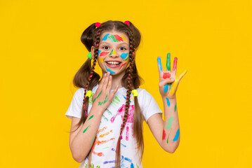 A young girl stained in multicolored paint shows four fingers and smiles broadly. Children's creativity. Yellow isolated background.