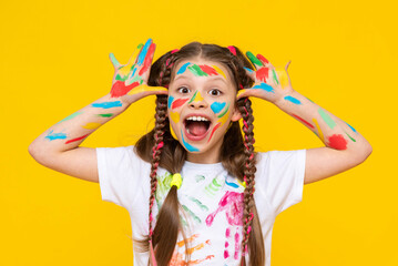 A young girl with brightly painted hands and multi colored pigtails shows her palms, smiling...