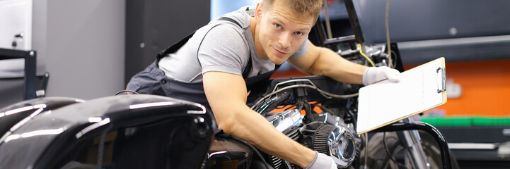 Male mechanic diagnoses modern motorcycle in service center. Concept of vehicle maintenance and transport insurance