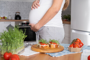 Pregnant young woman preparing healthy sandwiches with microgreens and vegetables. Food rich in fiber
