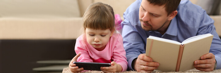 No more communication in family and dependence of children on gadgets. Dad holding book child is staring at smartphone screen - obrazy, fototapety, plakaty