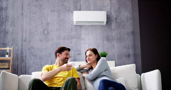 Happy Young Couple Adjusting Temperature Of Air Conditioner