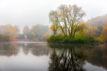 View of foggy lake, island and autumn color trees with reflection on water and copy space in clear sky. - 614234654
